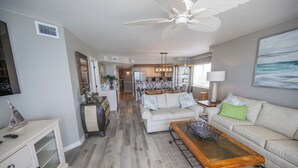 A spacious living room with a ceiling fan, a dining area with a chandelier, and a kitchen in the background.