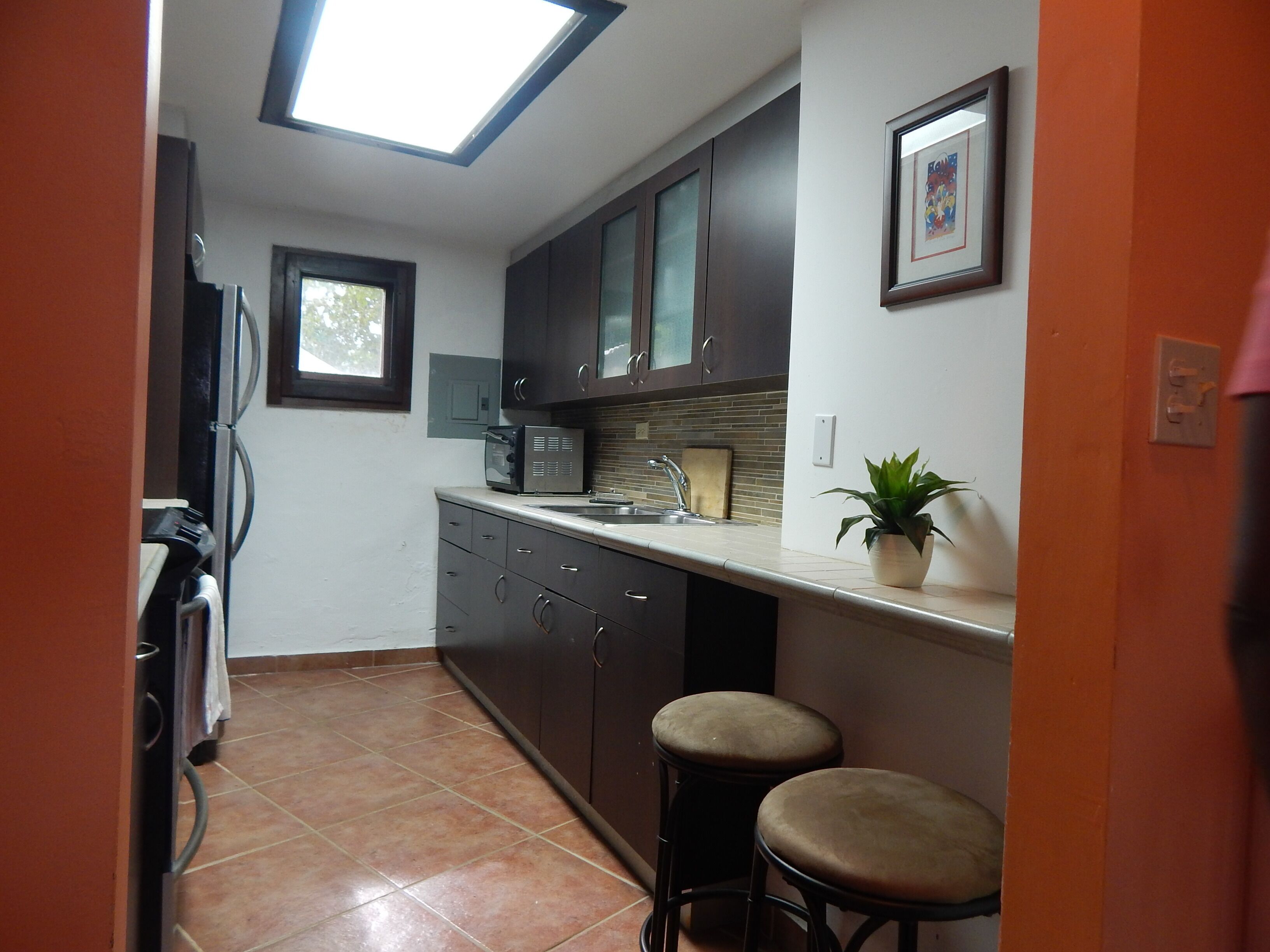 A compact kitchen with dark cabinets, a microwave, a sink, and two stools.