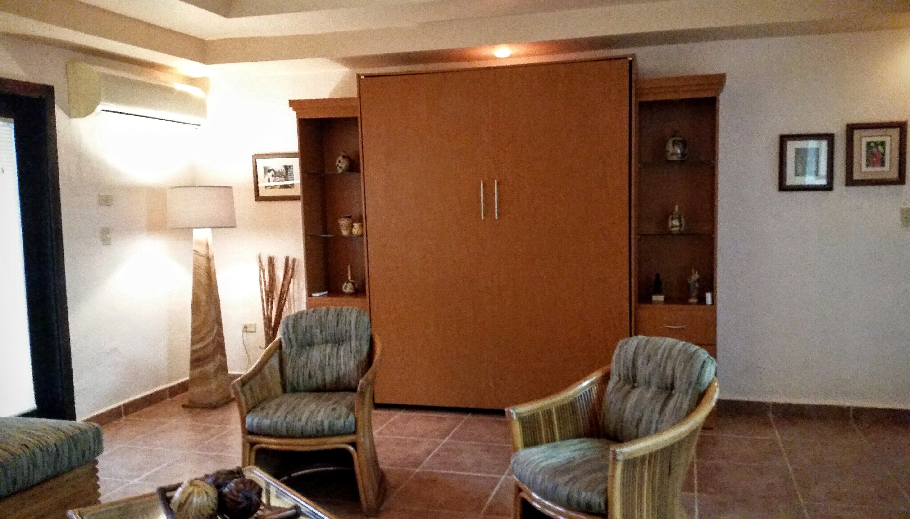 Una sala de estar con dos sillones, un aparador de madera con estantes y un armario grande.