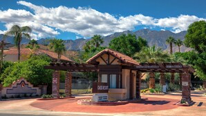 L’entrée d’un complexe hôtelier, avec une enseigne indiquant « Oasis Resort », un ciel dégagé et des montagnes en arrière-plan.