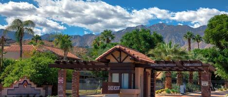 Entrada a un resort con un cartel que dice "Oasis Resort", cielo despejado y montañas al fondo.