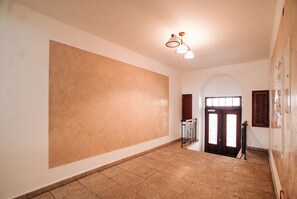 A spacious hallway with a large wall, a wooden door with glass panels, and a ceiling light fixture.