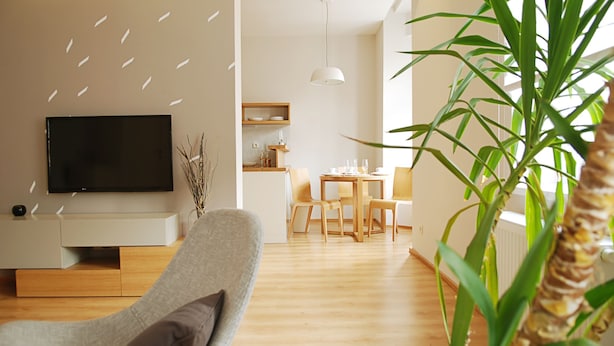 Una sala de estar moderna con un televisor de pantalla plana, un sofá gris y un comedor con muebles de madera.
