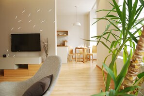 A modern living room with a flat-screen TV, a grey sofa, and a dining area with wooden furniture.