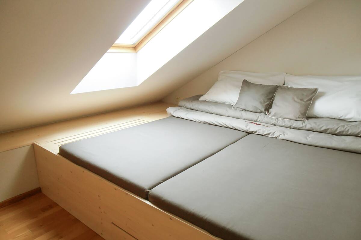A small, cozy room with a sloped ceiling and a skylight, featuring a bed with a mattress and pillows.