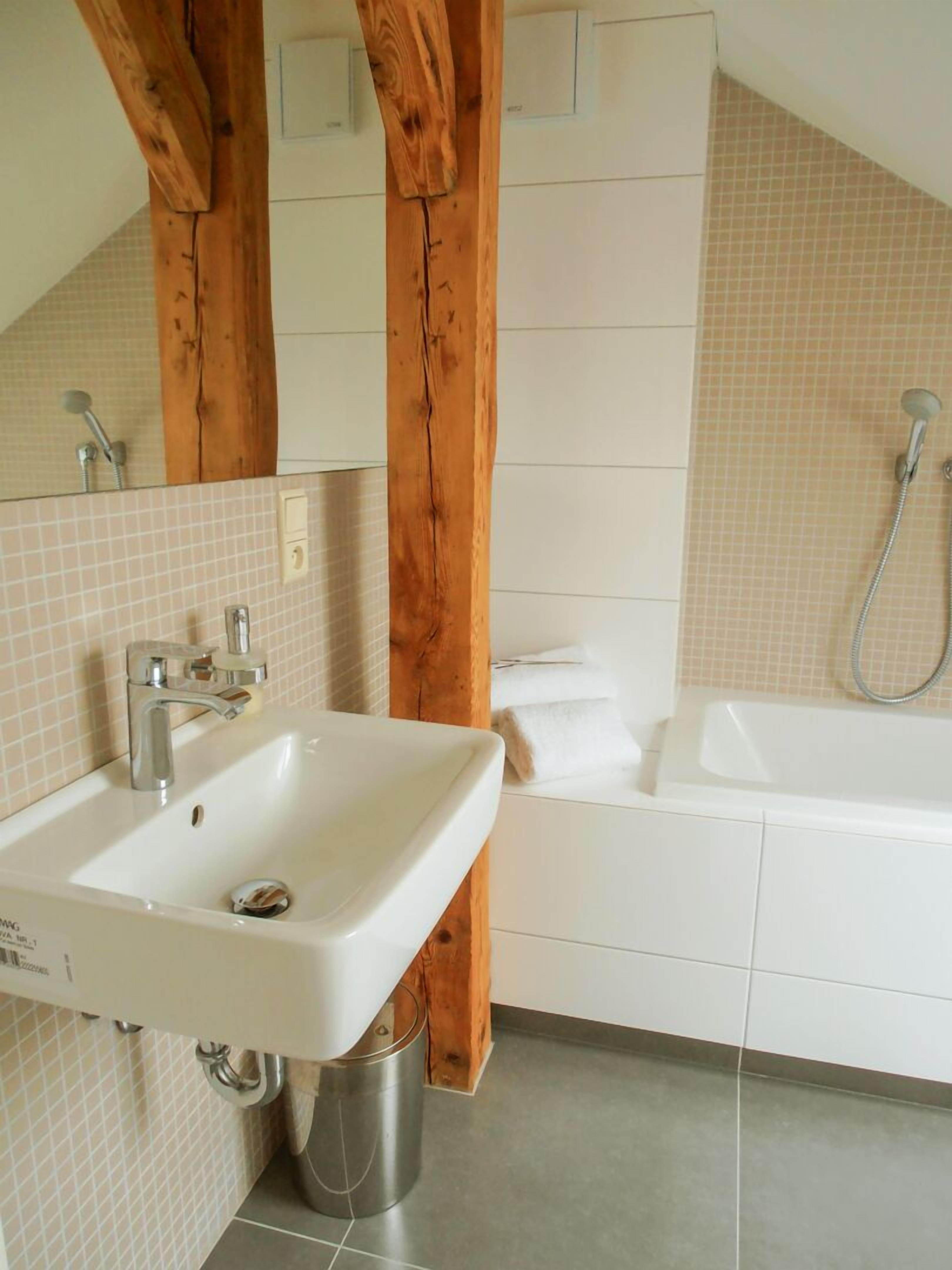 A bathroom with a white sink, a bathtub, and wooden beams.