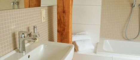 A bathroom with a white sink, a bathtub, and wooden beams.