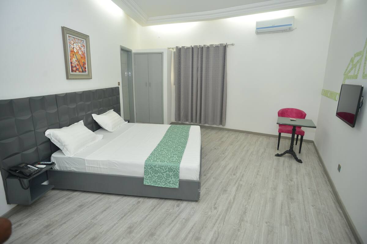 Quarto de hotel com cama, mesa de cabeceira, poltrona e escrivaninha com cadeira.