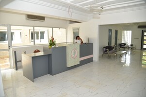 Zona de recepción con suelo de mármol, mostrador de recepción y área de estar con sillas.