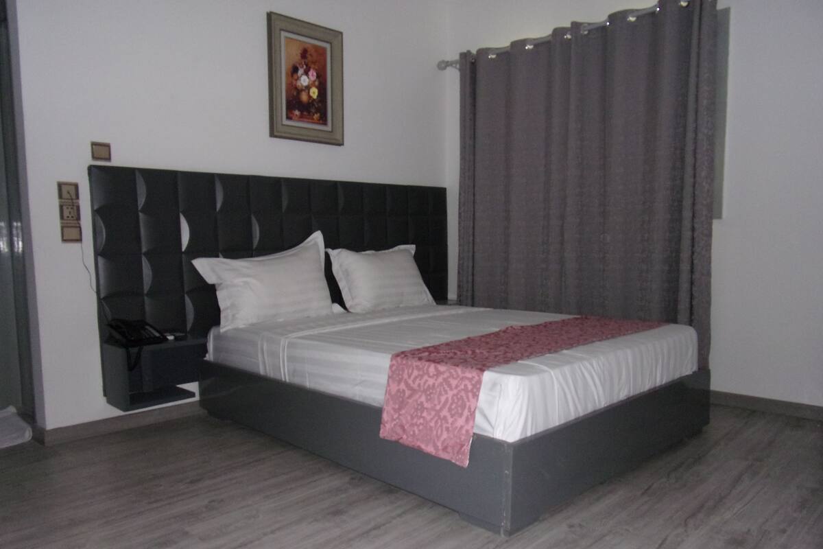 Quarto com cama, mesa de cabeceira, telefone, pintura na parede e cortina.