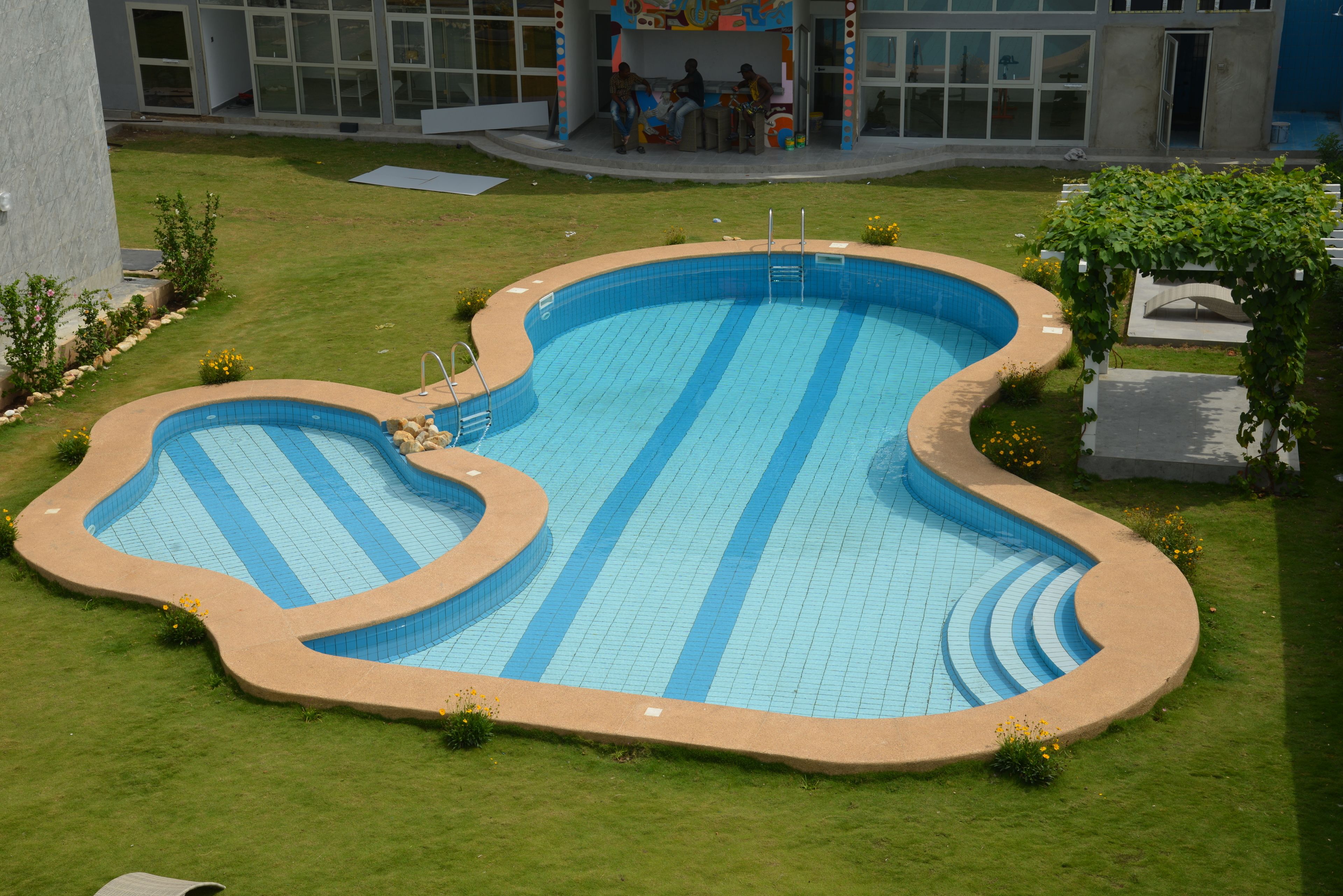 Une piscine à la forme originale, entourée d’une pelouse bien entretenue et, en arrière-plan, d’un bâtiment doté de grandes fenêtres.