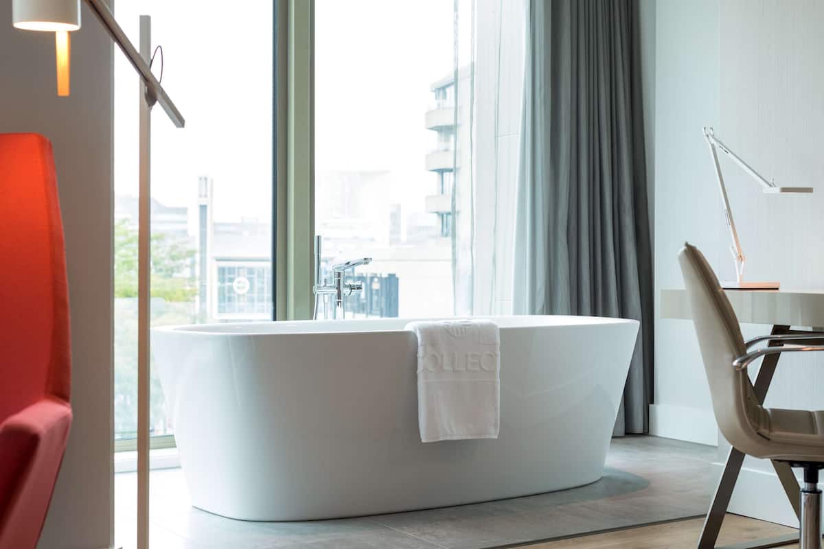 A modern bathroom with a freestanding bathtub, a red chair, and a desk with a lamp.
