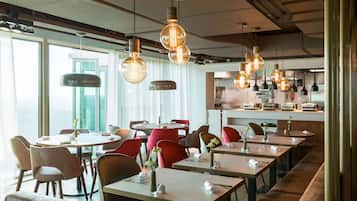 Un restaurante moderno con mesas redondas, sillas rojas y lámparas colgantes.
