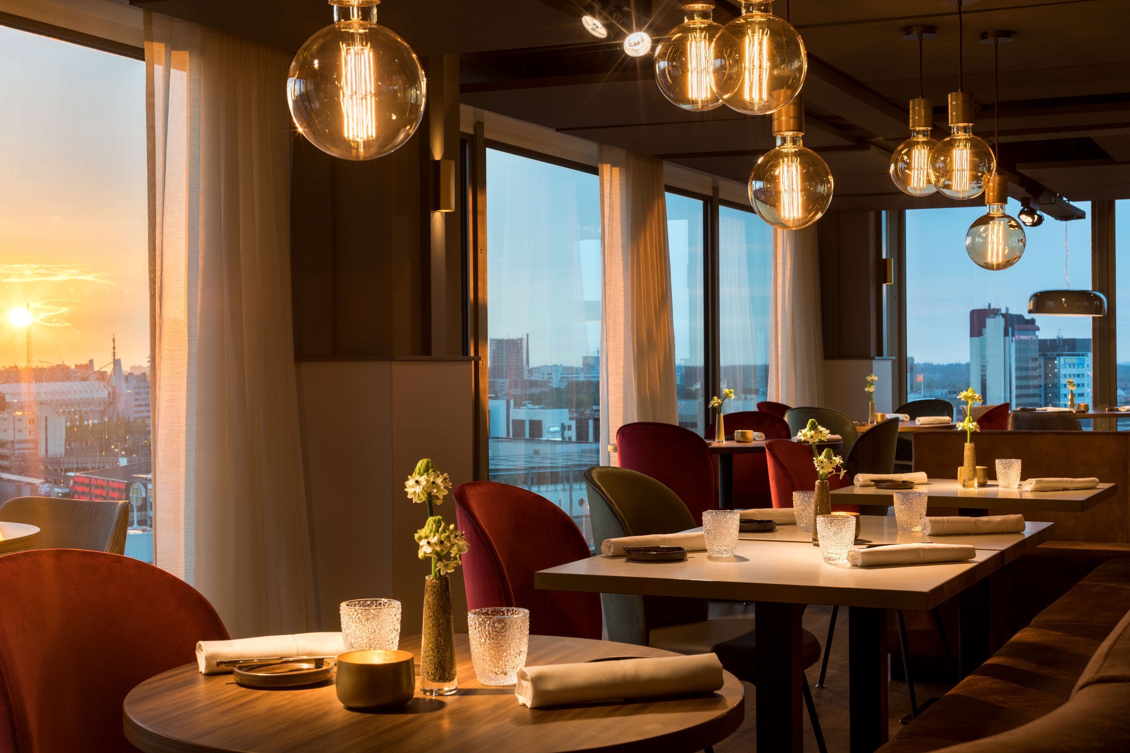 Un restaurant avec des tables rondes, des chaises rouges et des luminaires suspendus.