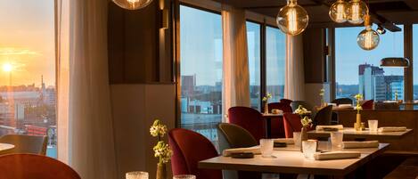 A restaurant with round tables, red chairs, and hanging light fixtures.