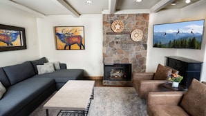 A living room with a stone fireplace, a large flat-screen TV, and artwork on the walls. - Landmark 404 - 2 Bedroom Diamond (Vail)