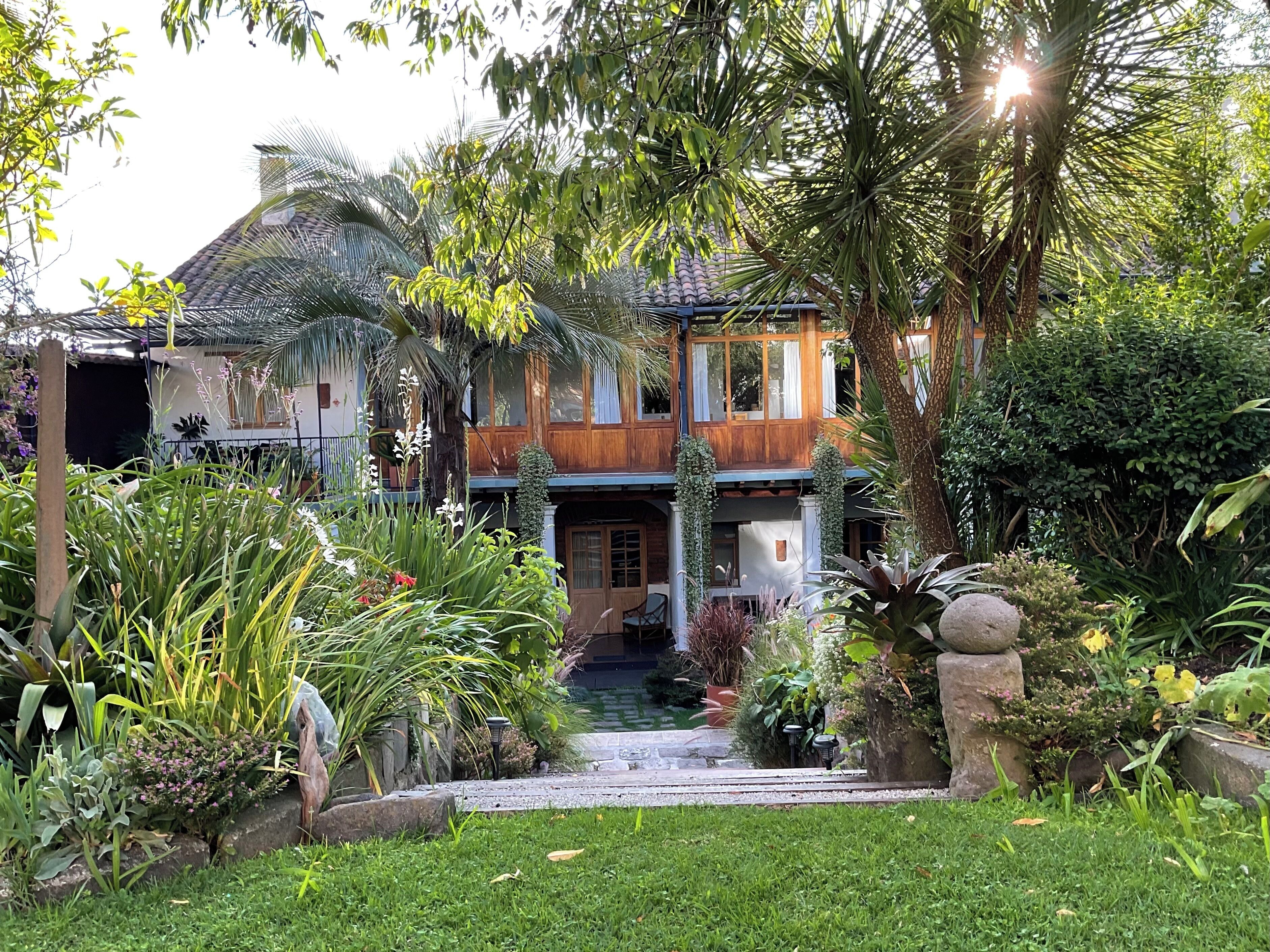 Une maison à deux étages avec une entrée donnant sur le jardin, entourée de différentes plantes et arbres.