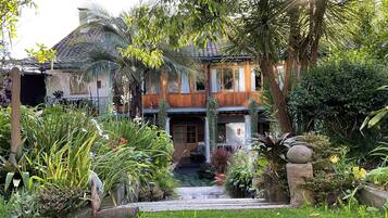 Une maison à deux étages avec une entrée donnant sur le jardin, entourée de différentes plantes et arbres.