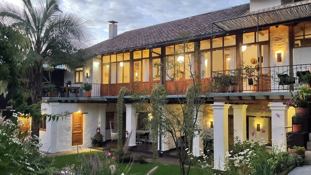 A two-story house with a balcony, large windows, and a garden with various plants and flowers. - modern Loft in historic Villa with beautiful gardens (Quito)
