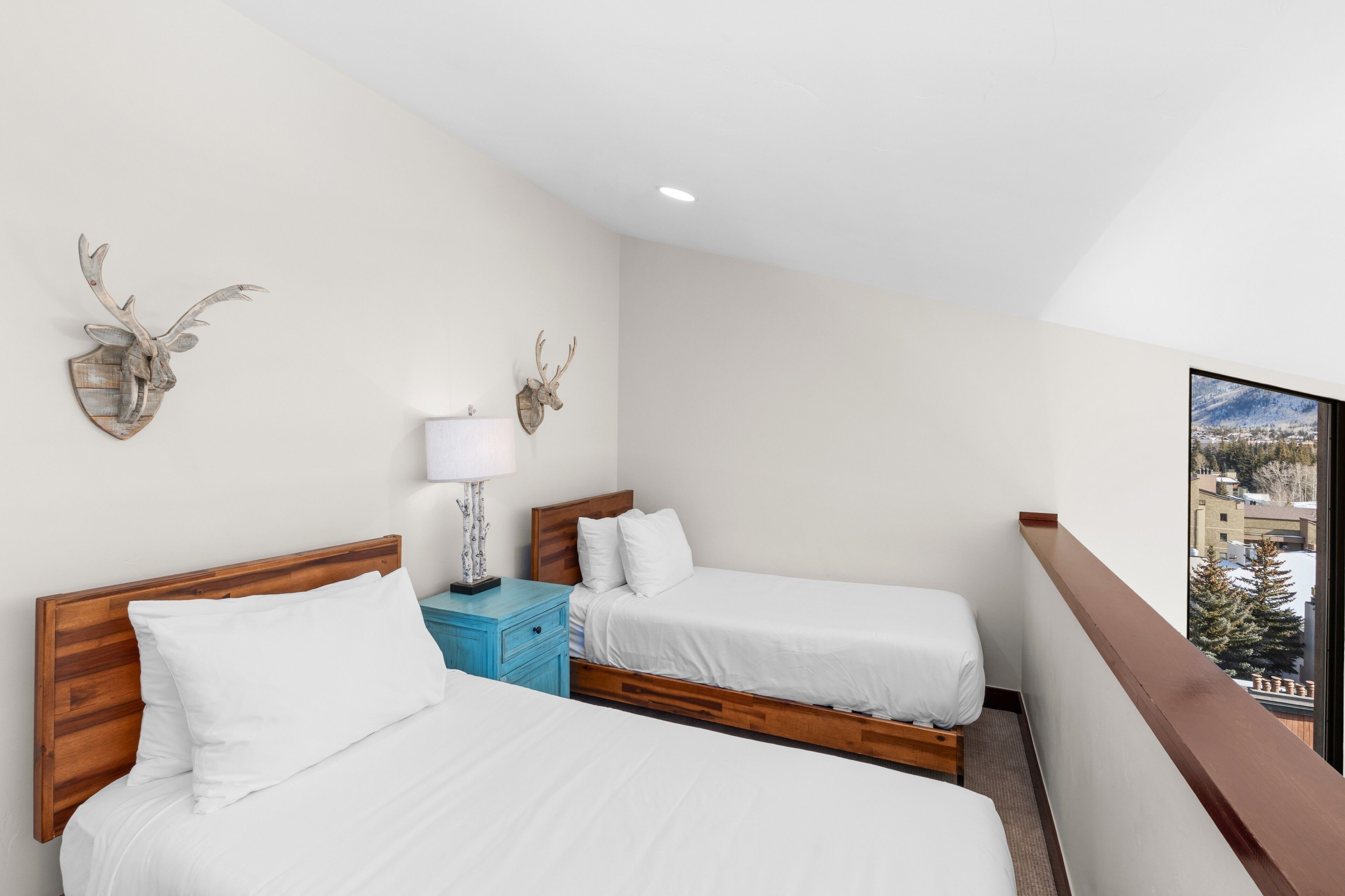 A hotel room with two beds, a wooden headboard, a nightstand with a lamp, and deer antler wall decorations.