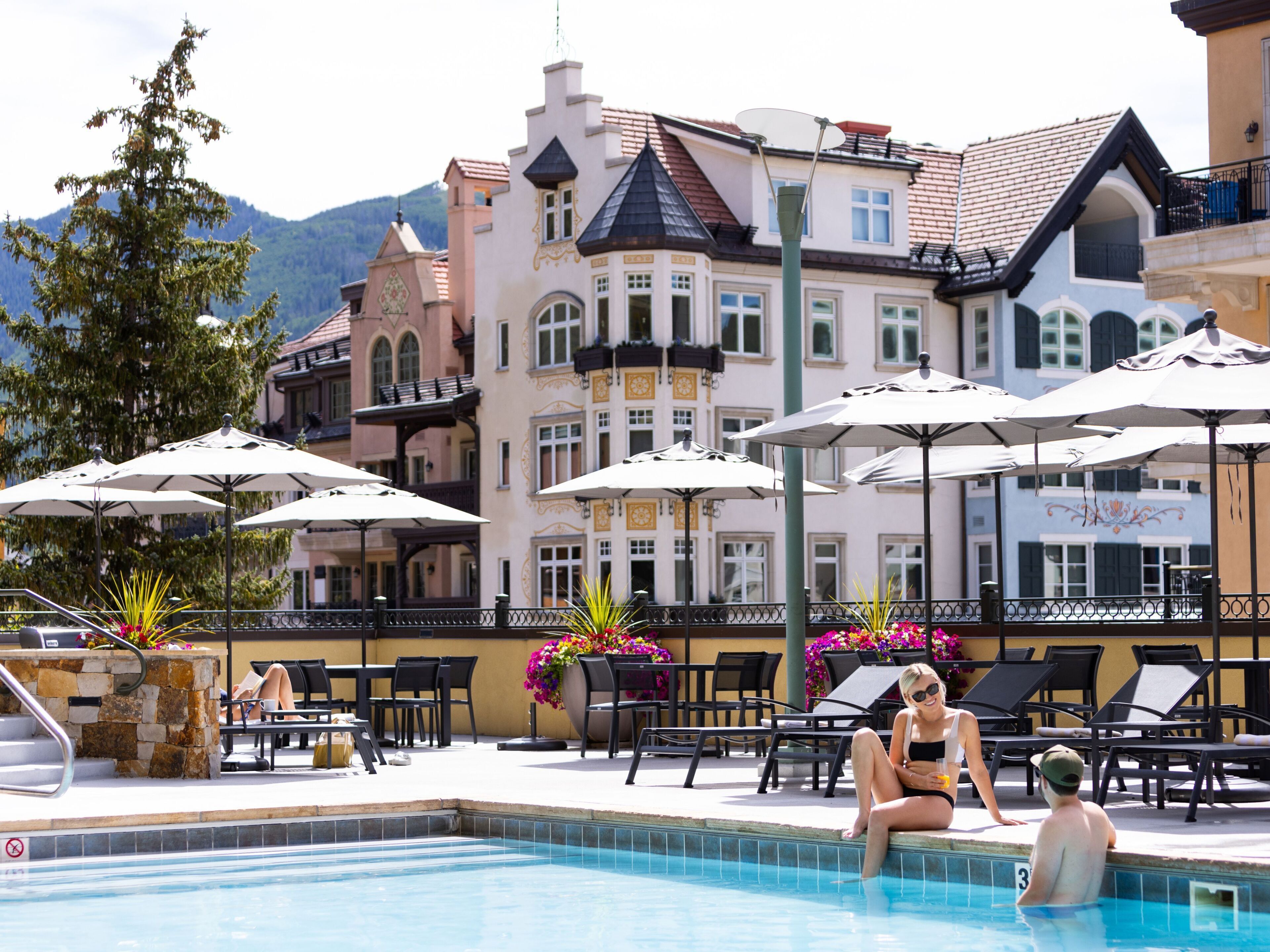 Charming alpine architecture provides a stunning backdrop to your sunny poolside retreat, where you can unwind on comfortable loungers under elegant umbrellas while taking in the mountain views and vibrant gardens.