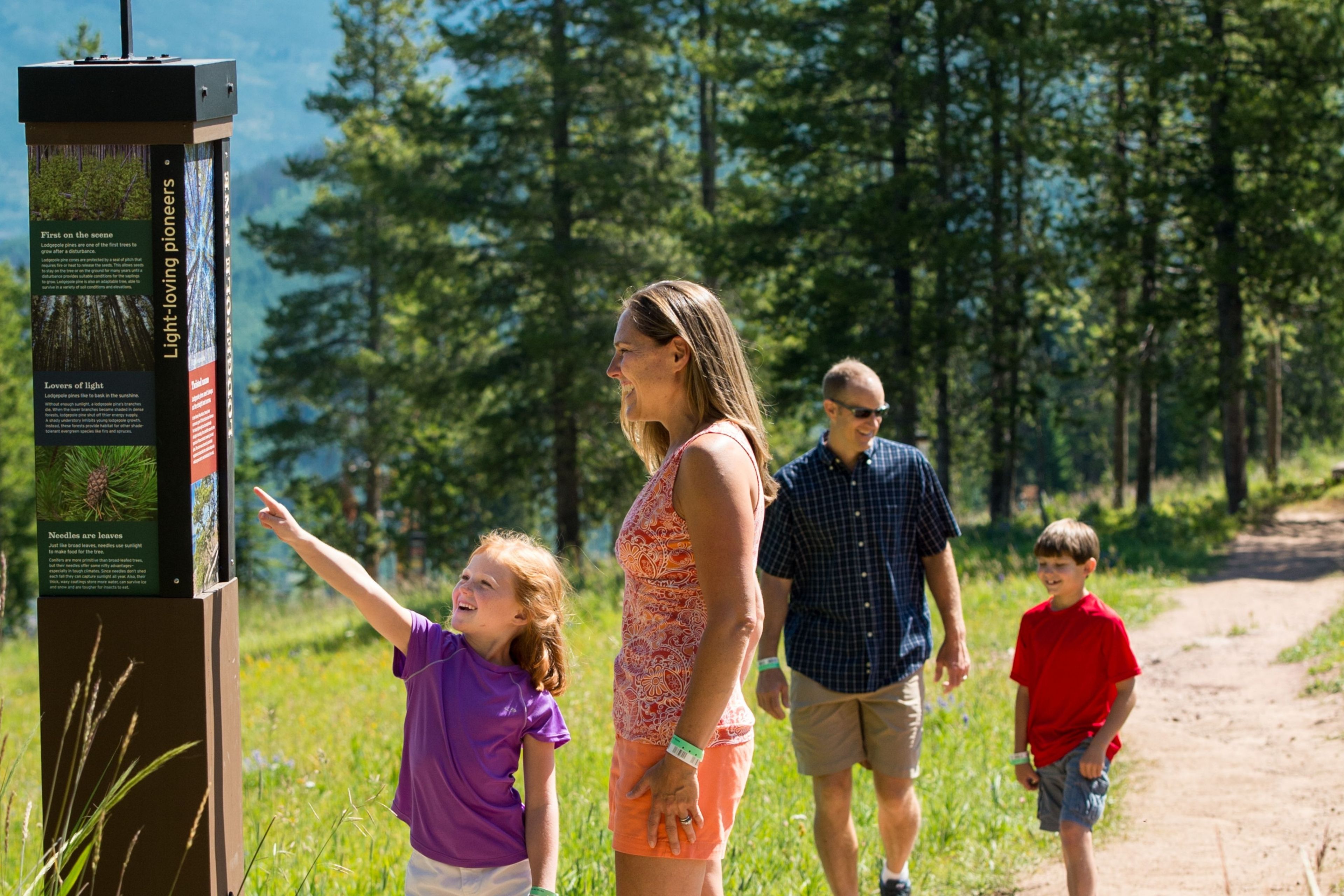 Eine Familie geht auf einem Pfad entlang, an dem ein Hinweisschild Informationen über die regionale Flora zeigt.