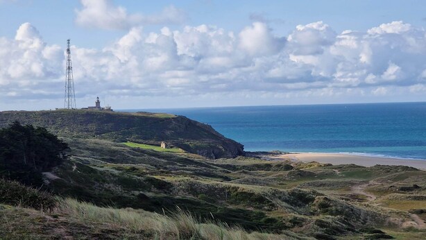 Un paisaje costero con un faro, terreno cubierto de hierba y una vista despejada del océano.