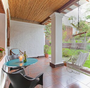 A covered patio with a table and chairs, a hanging chair, and a garden view. - Suite Tortuga with Beautiful Gardens in Historical Quito (Quito)