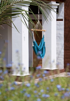 Relax in a serene outdoor haven with a hammock suspended between pillars, surrounded by a lush lawn and vibrant flowers.