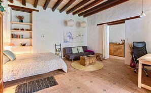 A cozy room with a bed, sofa, and a small wooden table. There is a bookshelf with books and decorative items, a painting on the wall, and a kitchen area with a chair and a table. - Suite Tortuga with Beautiful Gardens in Historical Quito (Quito)
