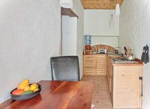 A compact kitchen with a wooden table, a bowl of fruit, a water dispenser, and a stove.