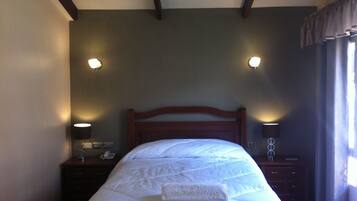 A neatly made bed with a pillow and a bedside table with a lamp and a phone.