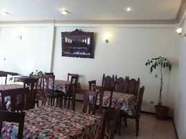 Un comedor con mesas y sillas de madera, un adorno en la pared y una planta en maceta.