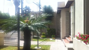 A residential building with a paved walkway, a palm tree, and a small garden with flowers. - El Prado Hotel (Cochabamba)
