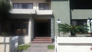 A multi-story building with a gated entrance, a staircase leading to the ground floor, and a small garden area with a palm tree. - El Prado Hotel (Cochabamba)