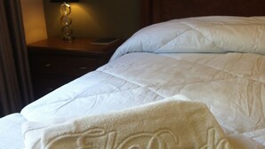 A neatly made bed with a white duvet and a folded towel with embossed text. - El Prado Hotel (Cochabamba)