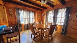 A wooden cabin interior with a dining table, chairs, and a ceiling fan.