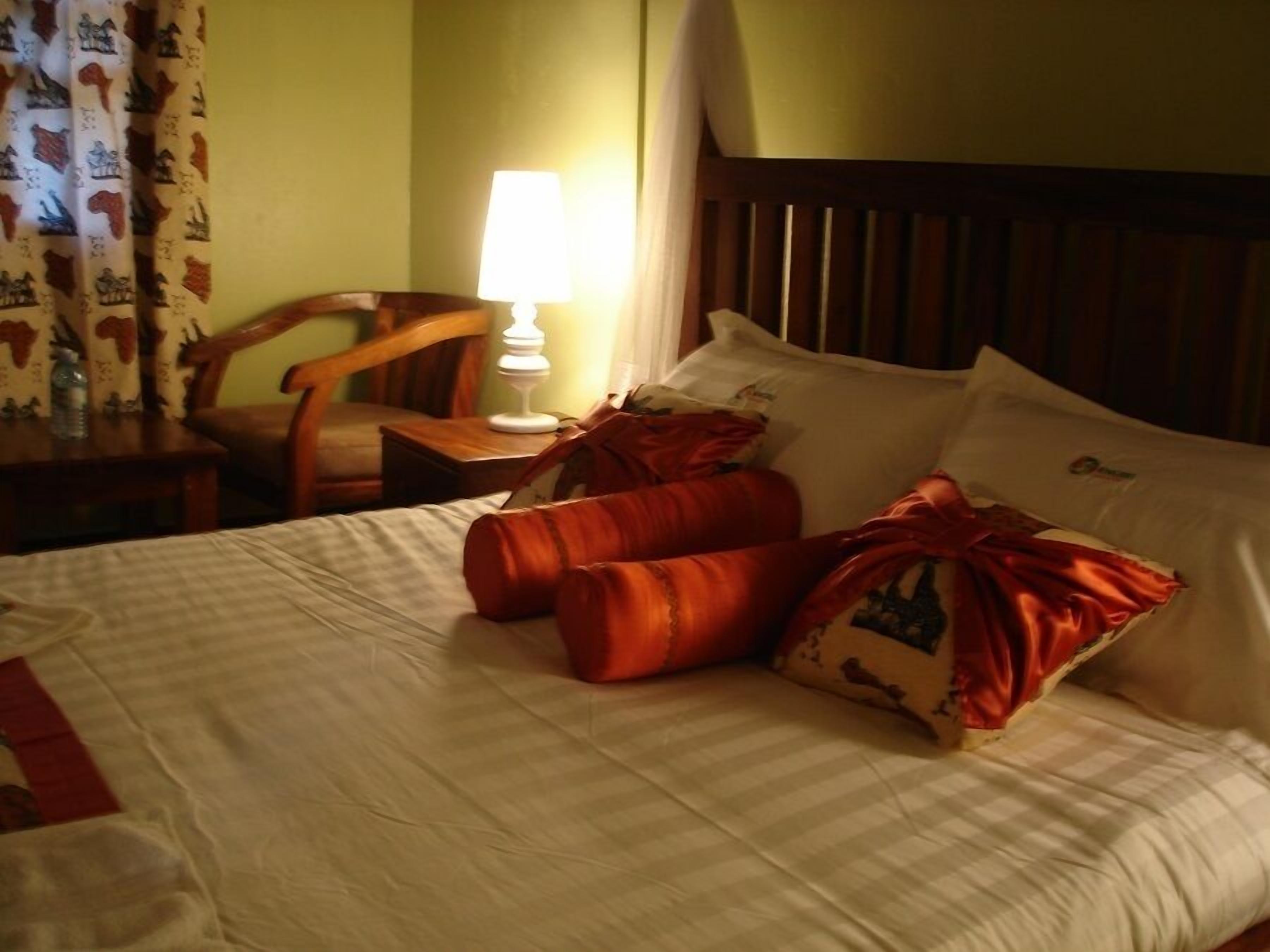 Ein Hotelzimmer mit einem Bett, Kissen, einem Nachttisch, einer Lampe, einem Sessel und Vorhängen.