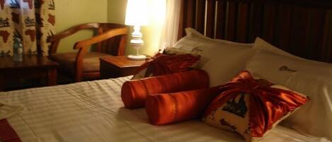 A hotel room with a bed, pillows, a nightstand, a lamp, a chair, and curtains.