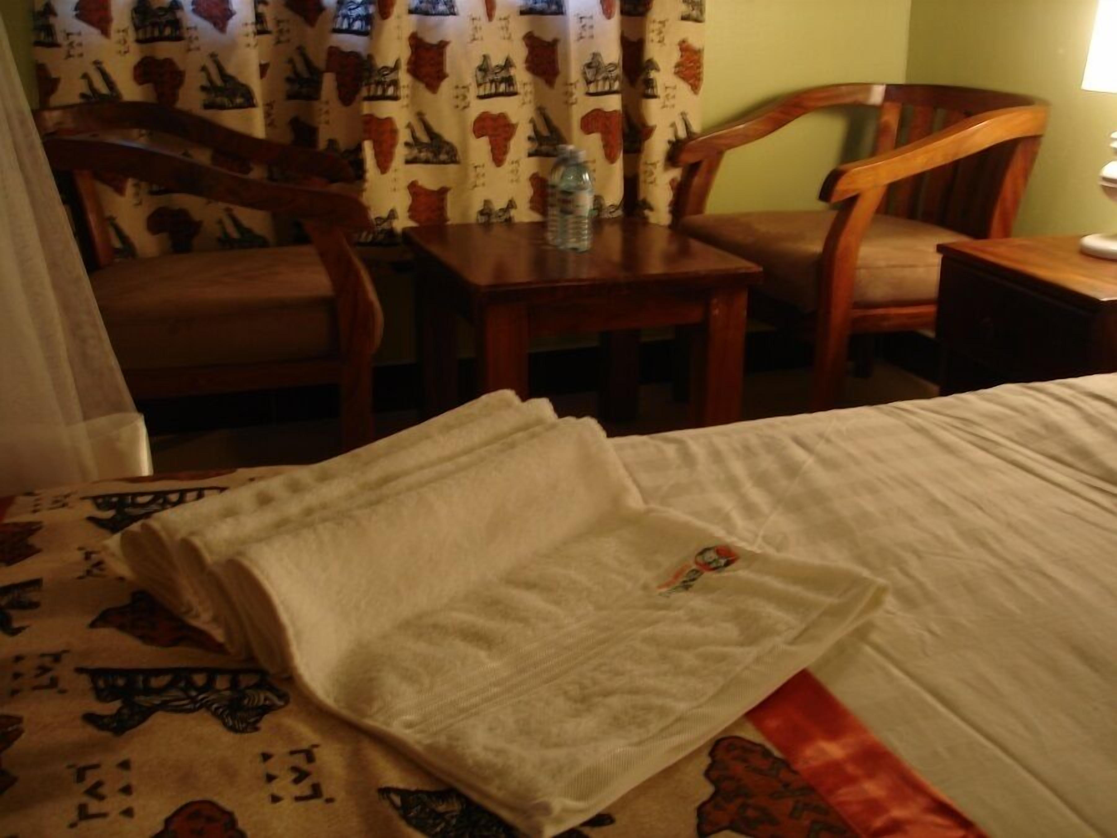 Een hotelkamer met een bed, twee houten stoelen, een klein tafeltje en een gordijn met dierenprint.