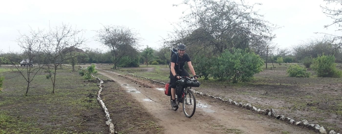 Een persoon fietst op een onverhard pad, omringd door begroeiing en bomen.