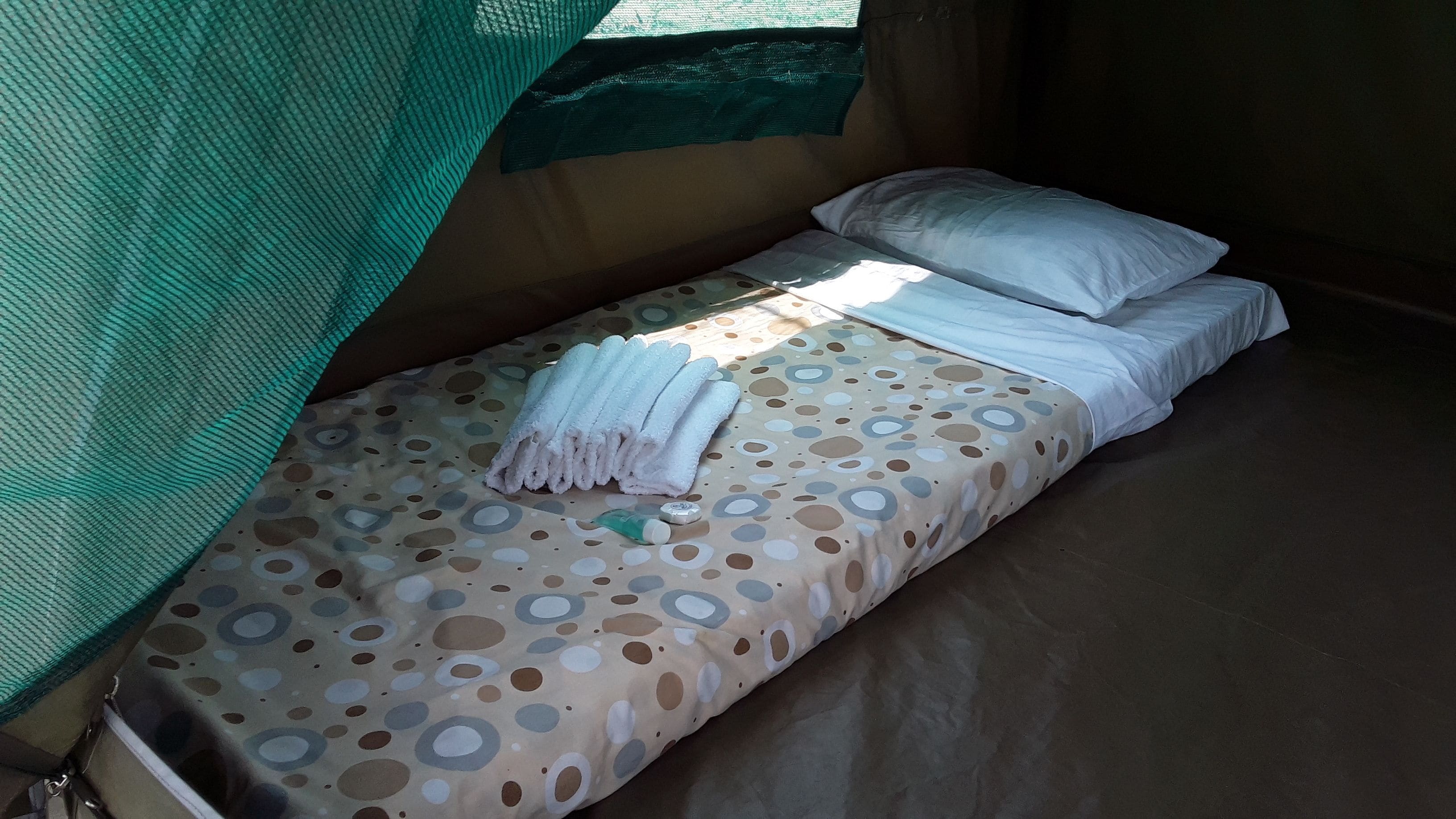 Ein Einzelbett mit einem gemusterten Bettbezug, weißen Kissen und einem gefalteten Handtuch.