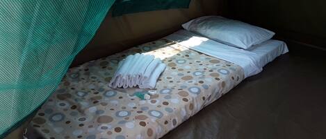 Ein Einzelbett mit einem gemusterten Bettbezug, weißen Kissen und einem gefalteten Handtuch.
