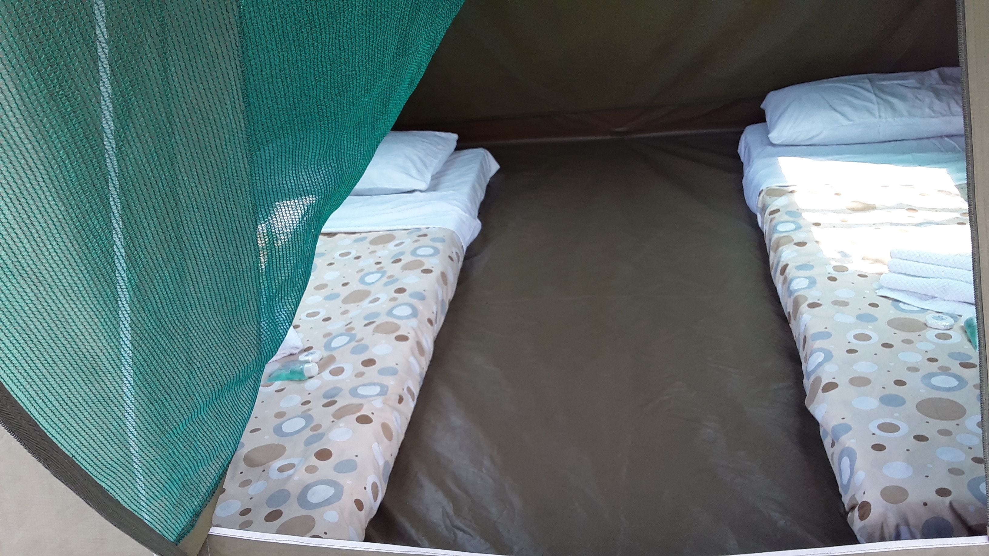 A single bed with a patterned bedspread, a green mosquito net, and white pillows.