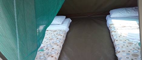 A single bed with a patterned bedspread, a green mosquito net, and white pillows.