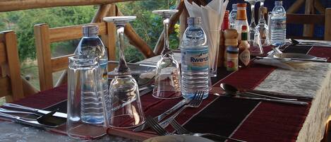 A table set outdoors with clear glass bottles, cutlery, and a bottle of Rwenzu water.