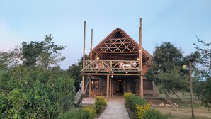 Una estructura de madera con techo de paja, rodeada de follaje y un camino pavimentado.
