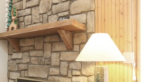 A stone fireplace with a mantel shelf, a table with a lamp, and a wooden wall panel.