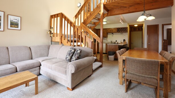 A spacious living room with a wooden staircase, a dining area, and a kitchen in the background.