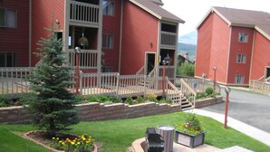 A red building with a balcony and a small tree in the front yard.